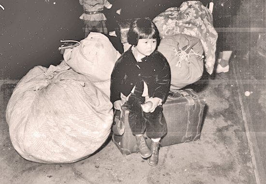 Photo of a young evacuee of Japanese ancestry waiting with the family baggage before leaving by bus for an assembly center in the spring of 1942